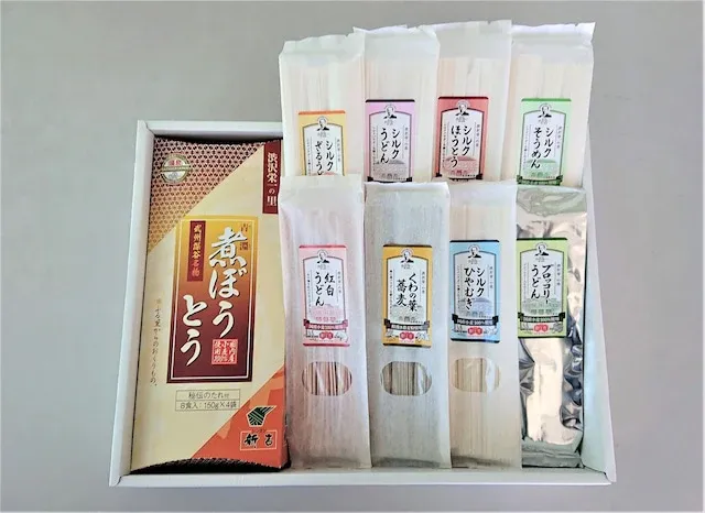 新吉製麺所のギフトセットの写真。化粧箱に、煮ぼうとうの箱と、シルクざるうどん・シルクうどん・シルクほうとう・シルクそうめん・紅白うどん・そば・シルクひやむぎ・ブロッコリーうどんの8種の麺が並んでいる。